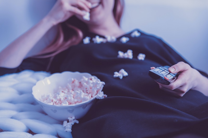 Kvinna tittar p tv och käkar popcorn
